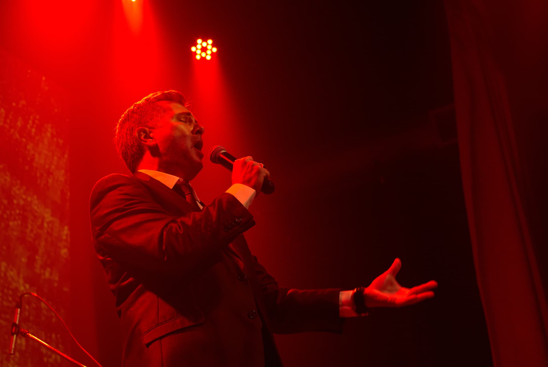 Christian Valverde cantando con micrófono bajo luces rojas de teatro
